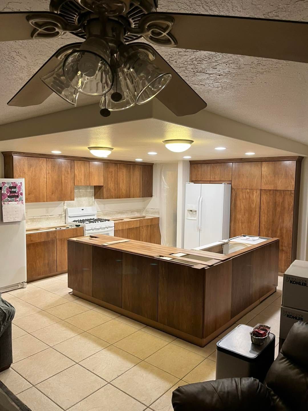 Open kitchen with wood cabinets, white appliances, central island, and ceiling fan under vaulted ceiling.