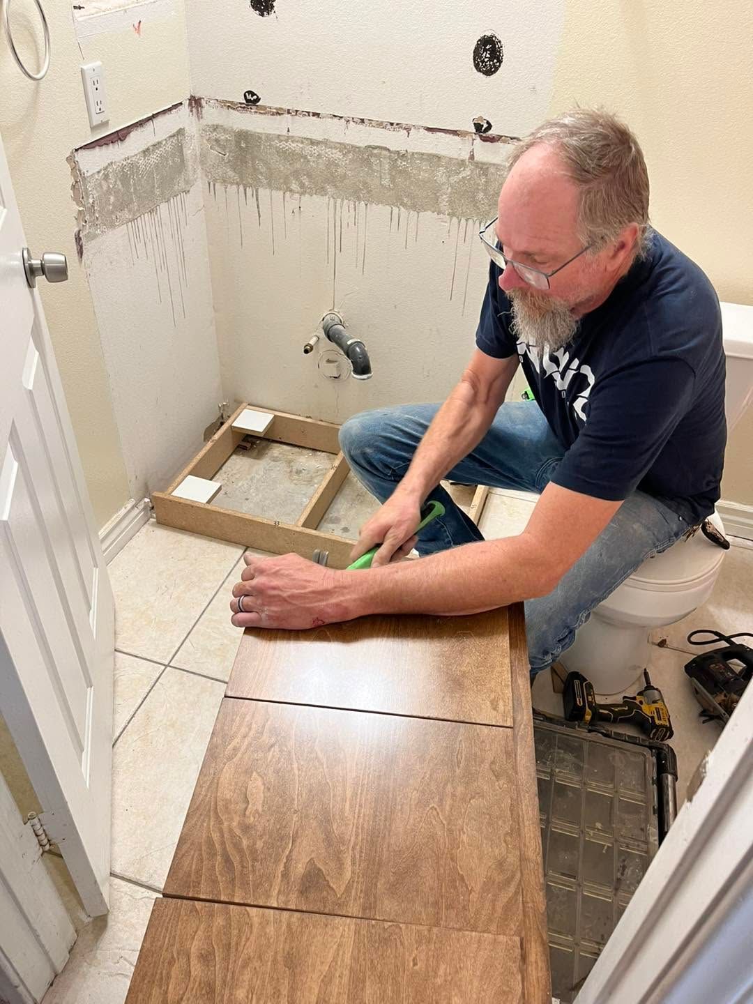 Man installing wood-look flooring in a small bathroom under renovation