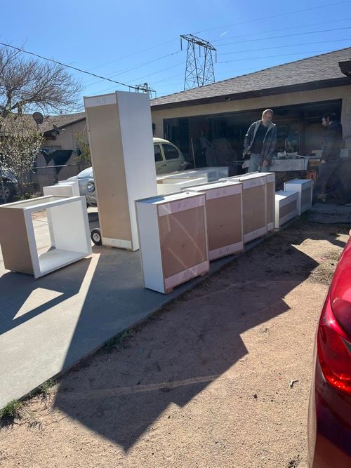 Appliances and cabinets arranged in a driveway beside a house, with a person standing nearby.