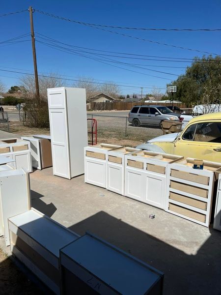 White kitchen cabinets and a tall cabinet outdoors on a driveway, with a yellow car in the background.