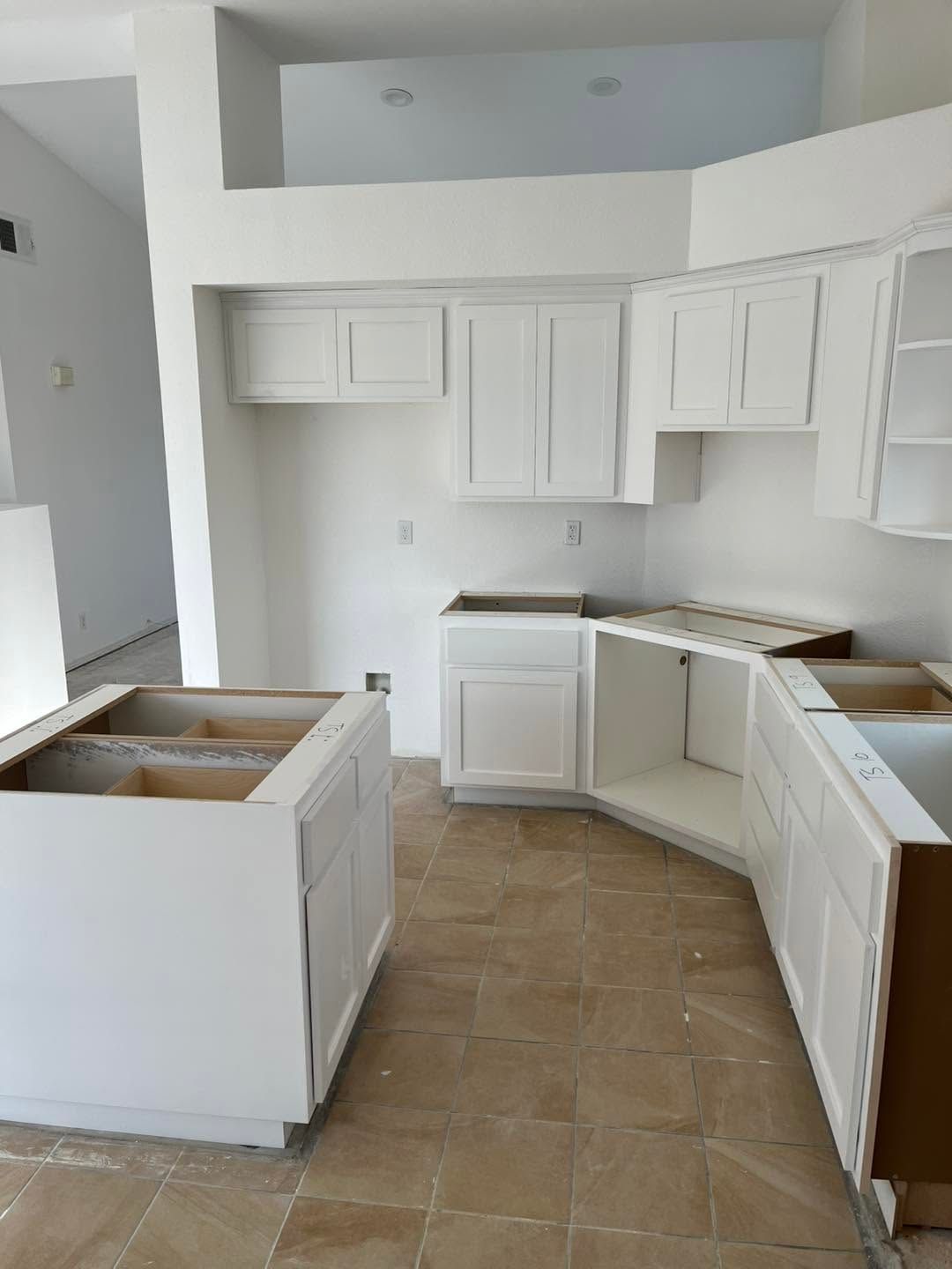 White kitchen under renovation with unfinished cabinets and tan tile floor