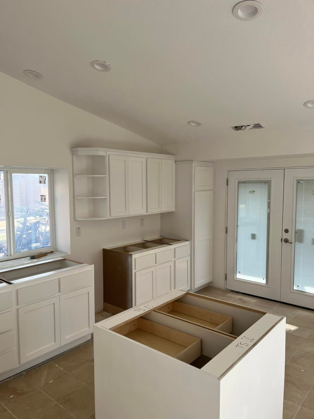 Bright white kitchen under renovation with unfinished island cabinets and french doors.