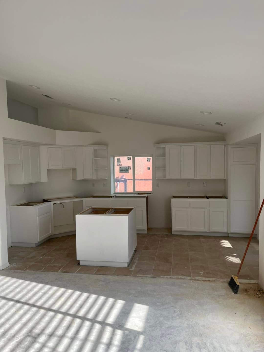 Unfinished kitchen with white cabinets, center island, and sunlight casting shadows across the floor.