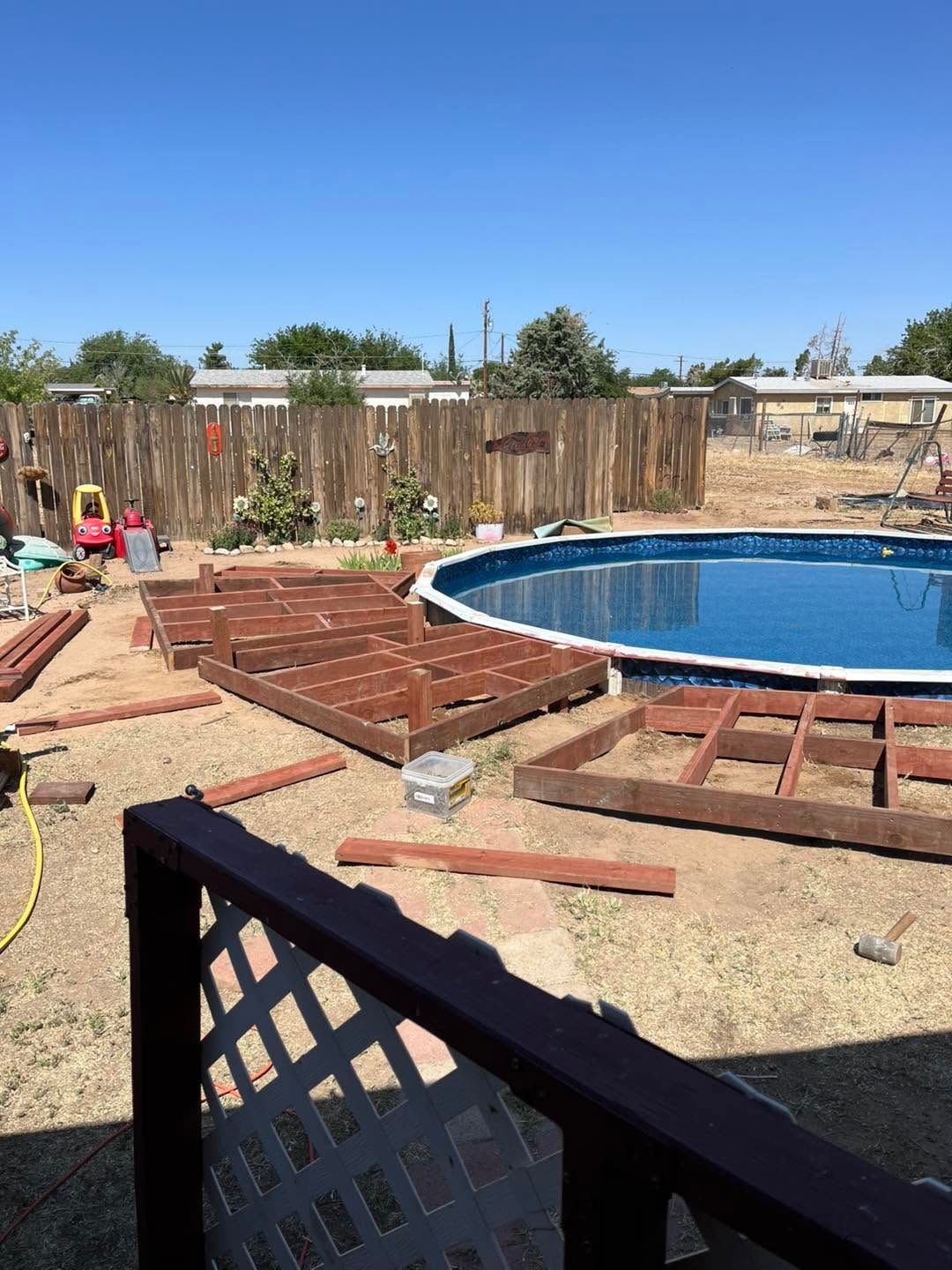 Backyard pool under construction with wooden framing and stacked lumber beside a round blue pool