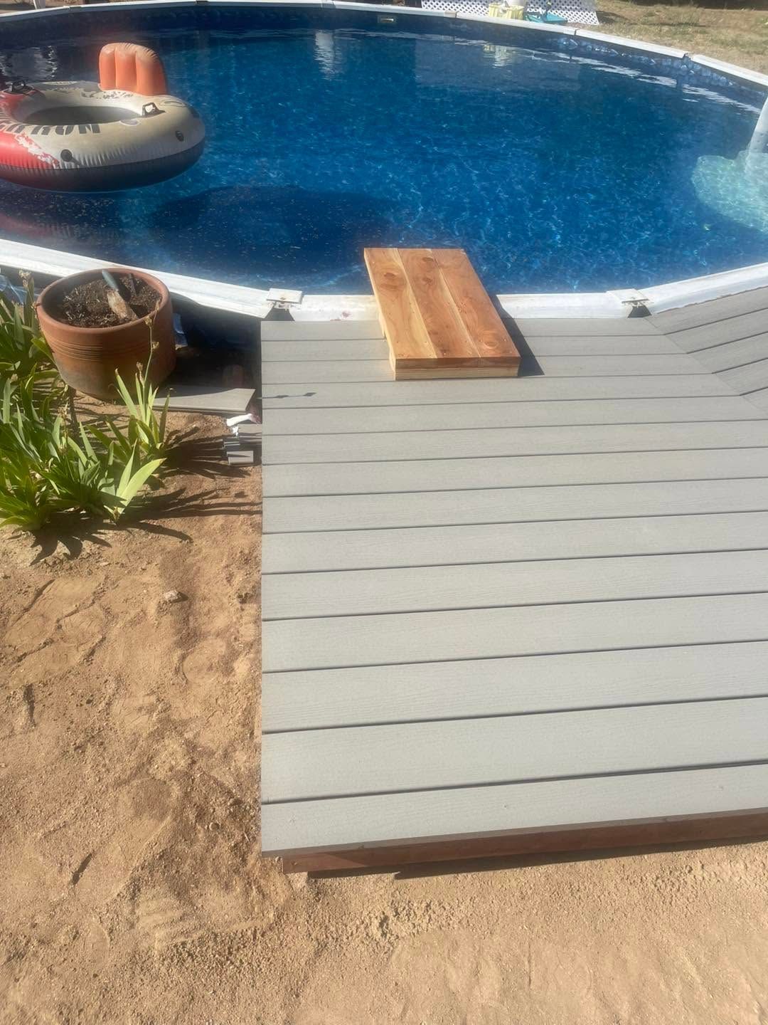 Backyard pool with gray ramp, small wooden board, potted plants, and an inflatable raft in blue water