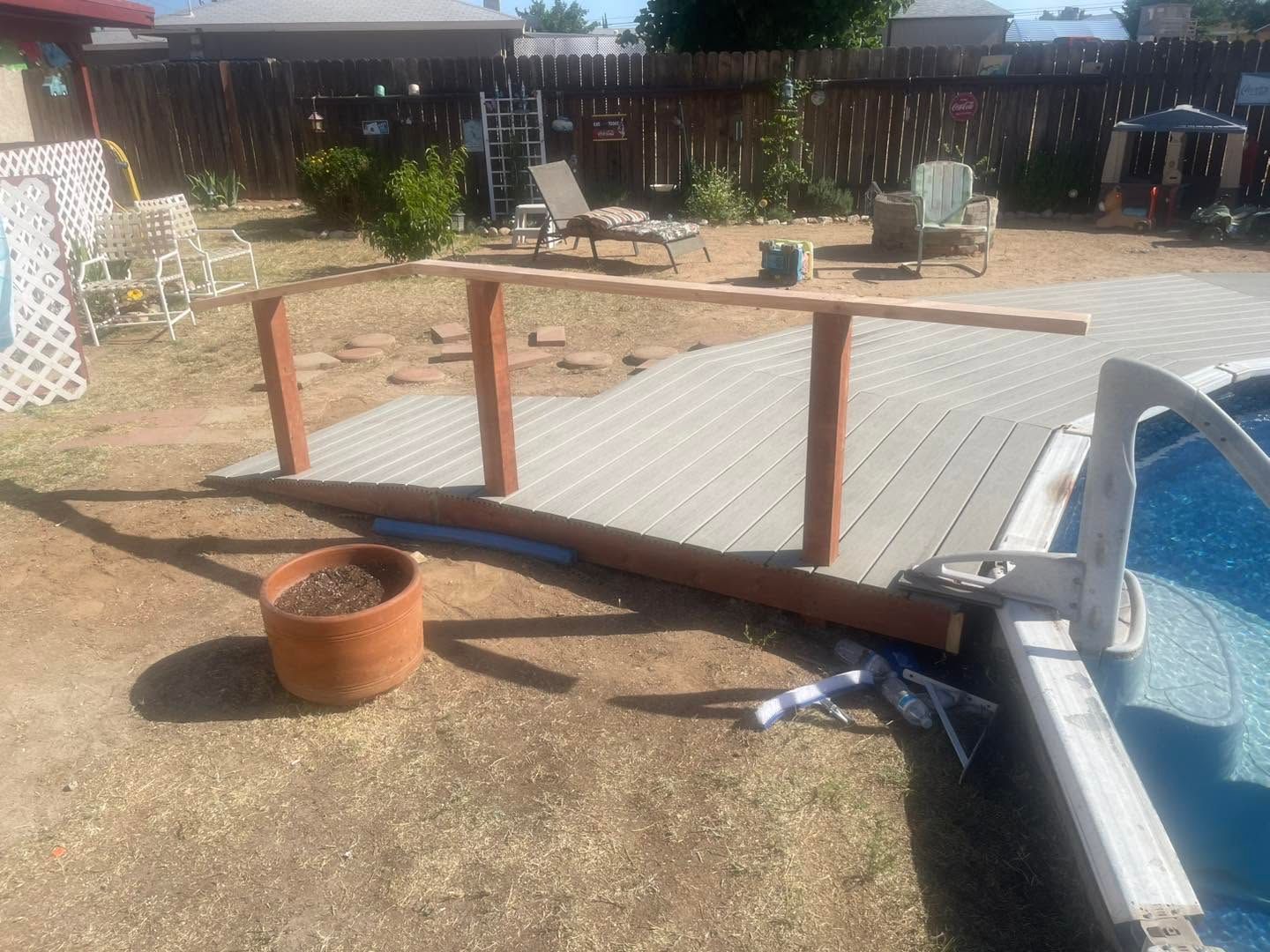 Backyard deck ramp under construction beside an above-ground pool, with wooden rail posts and a garden pot.