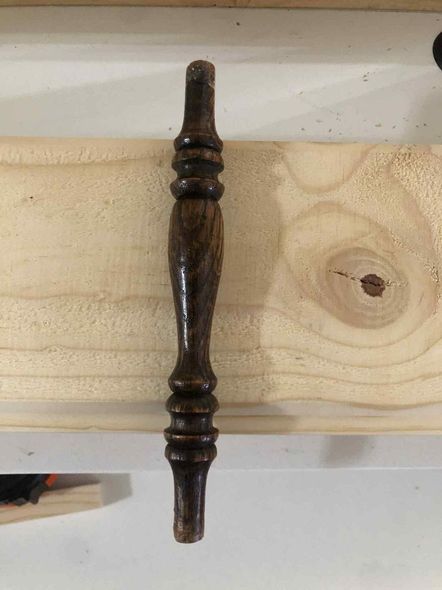 Dark wooden turned spindle laid horizontally on a light wood board.