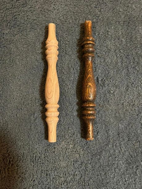 Two carved wooden spindles, one light and one dark, on a gray carpet.
