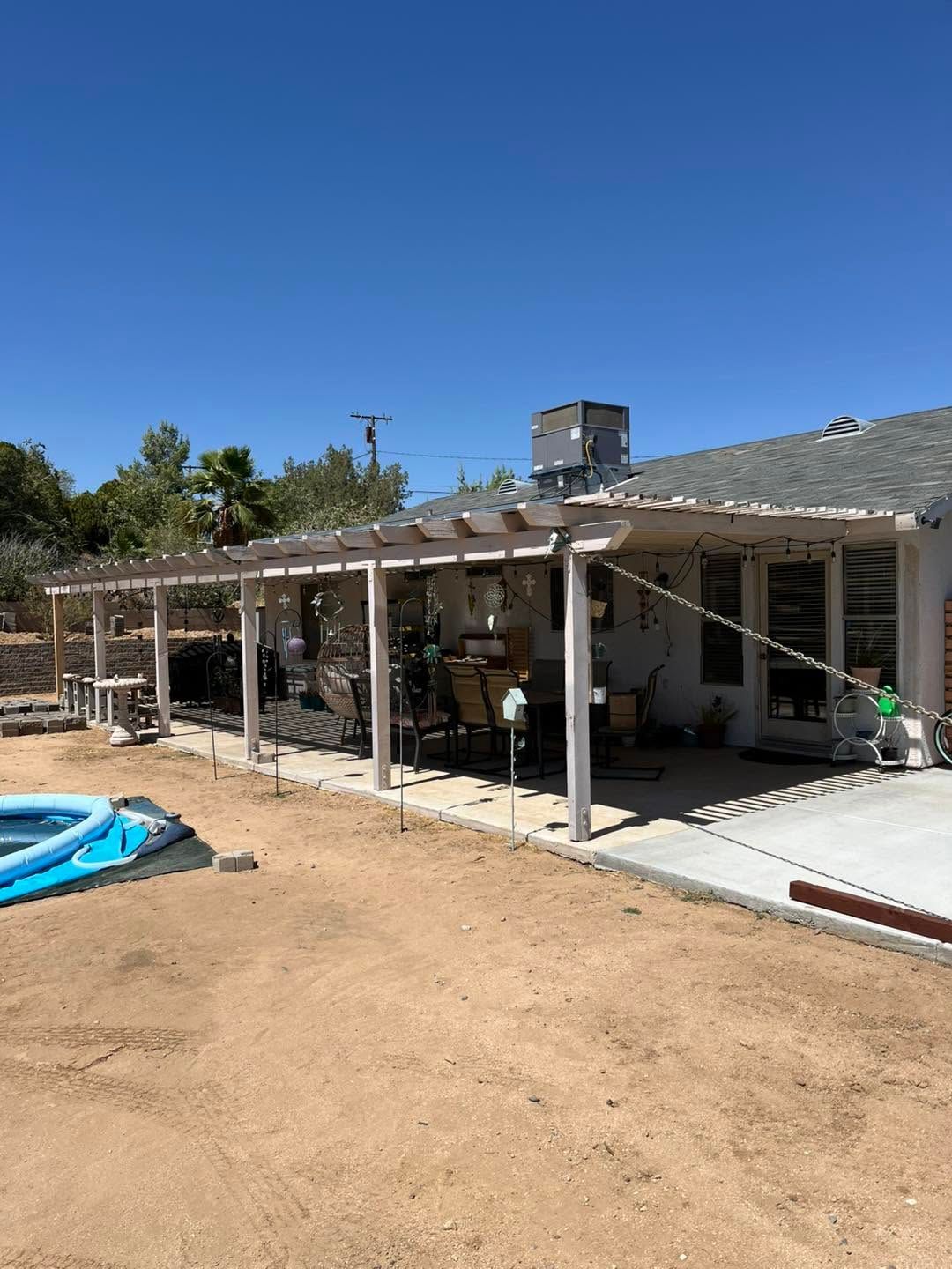 Backyard patio with white pergola, dirt yard, above-ground pool, and clear blue sky