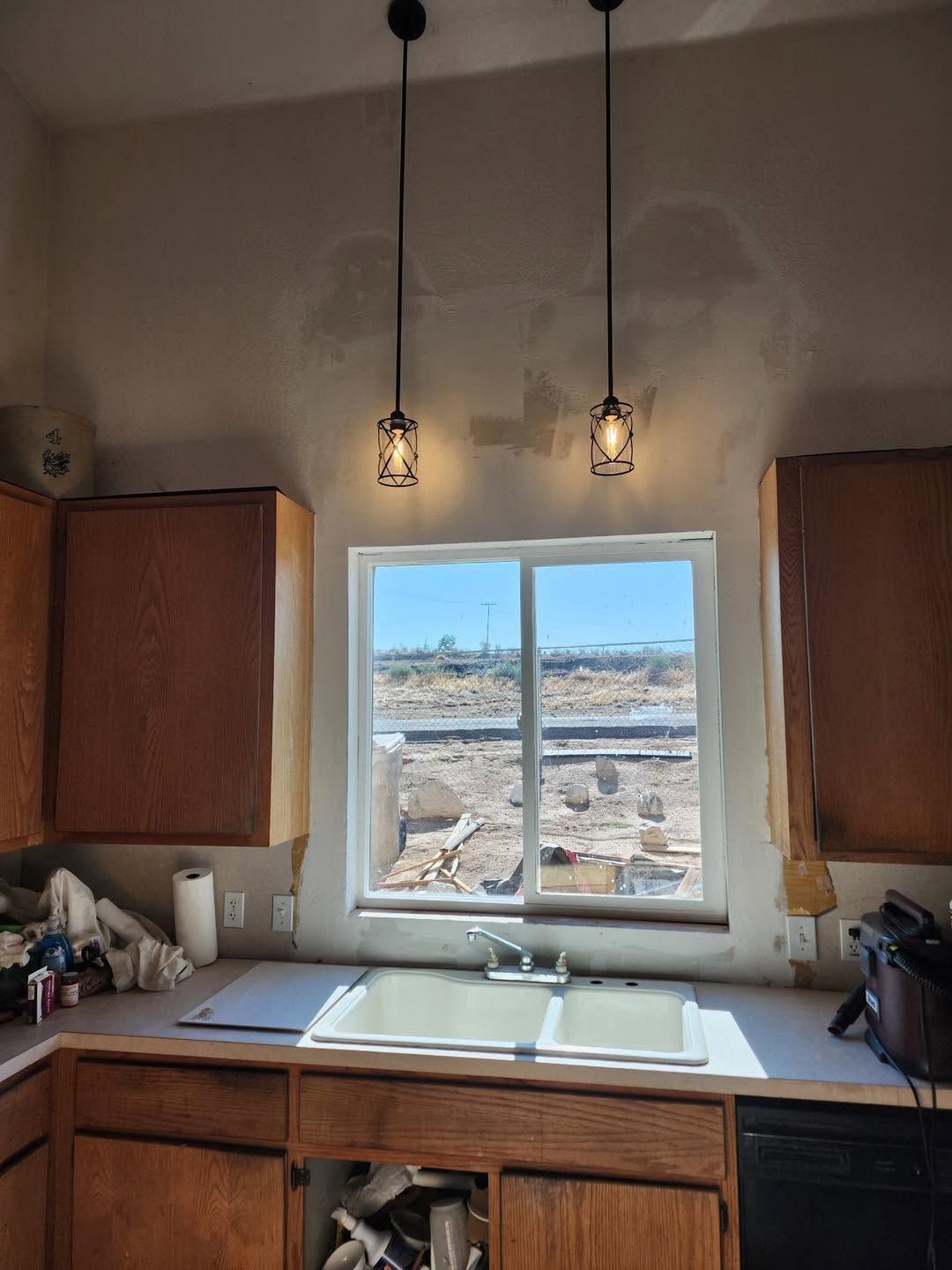 Kitchen sink beneath a window, with wood cabinets and two hanging pendant lights.