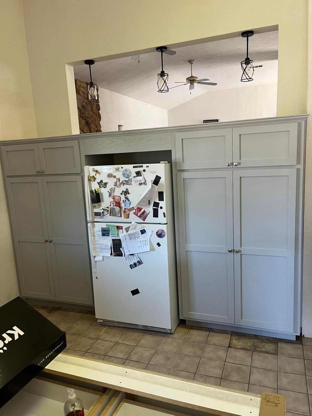 Kitchen with white refrigerator and gray cabinets beneath a pass-through opening to a dining area.
