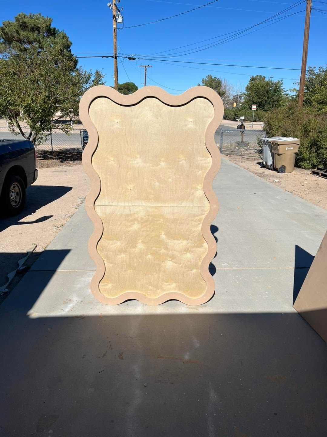 Wooden board with wavy edges standing outdoors on a sunny driveway in a residential area