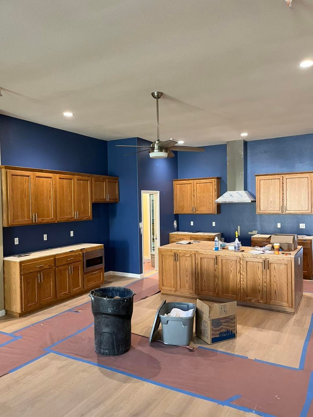 Kitchen under renovation with blue walls, wooden cabinets, island, and construction supplies on the floor
