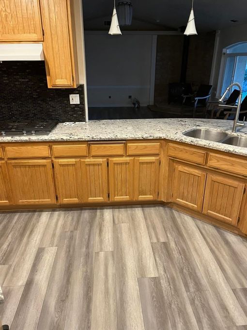 Kitchen with wood cabinets, granite countertop, black backsplash, and light wood flooring opening to a dining area