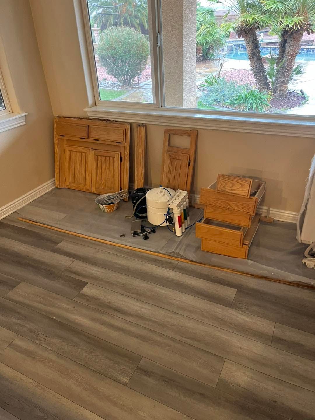 Furniture and boxes lined up by a window in an empty room, with tools on the floor.