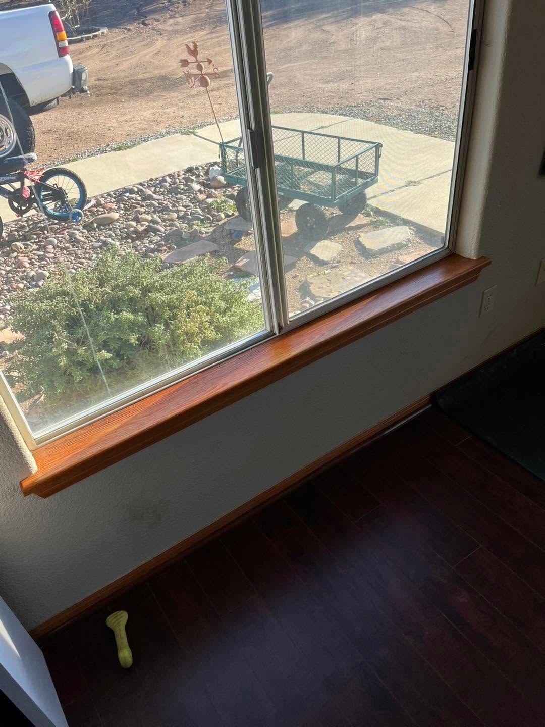 View through a window of a driveway with a small green cart and a partial motorcycle; wooden window sill in foreground