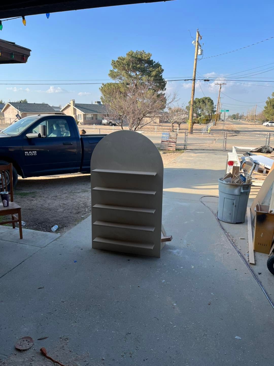 Gray arched storage cabinet on a concrete driveway with a blue pickup truck and trash cans nearby