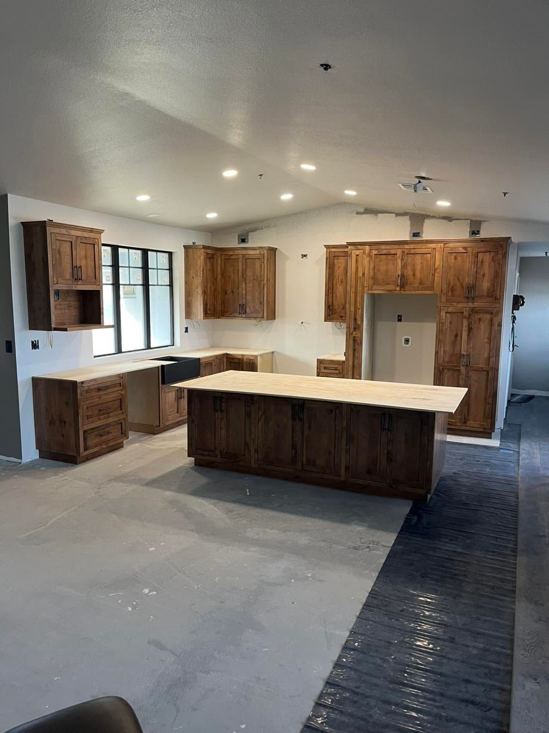Modern kitchen with white walls, wood cabinets, central island, and unfinished floor under bright ceiling lights