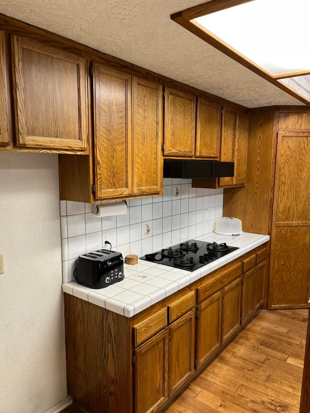 Wood-paneled kitchen with white tile backsplash, wooden cabinets, stove, toaster oven, and hardwood floor