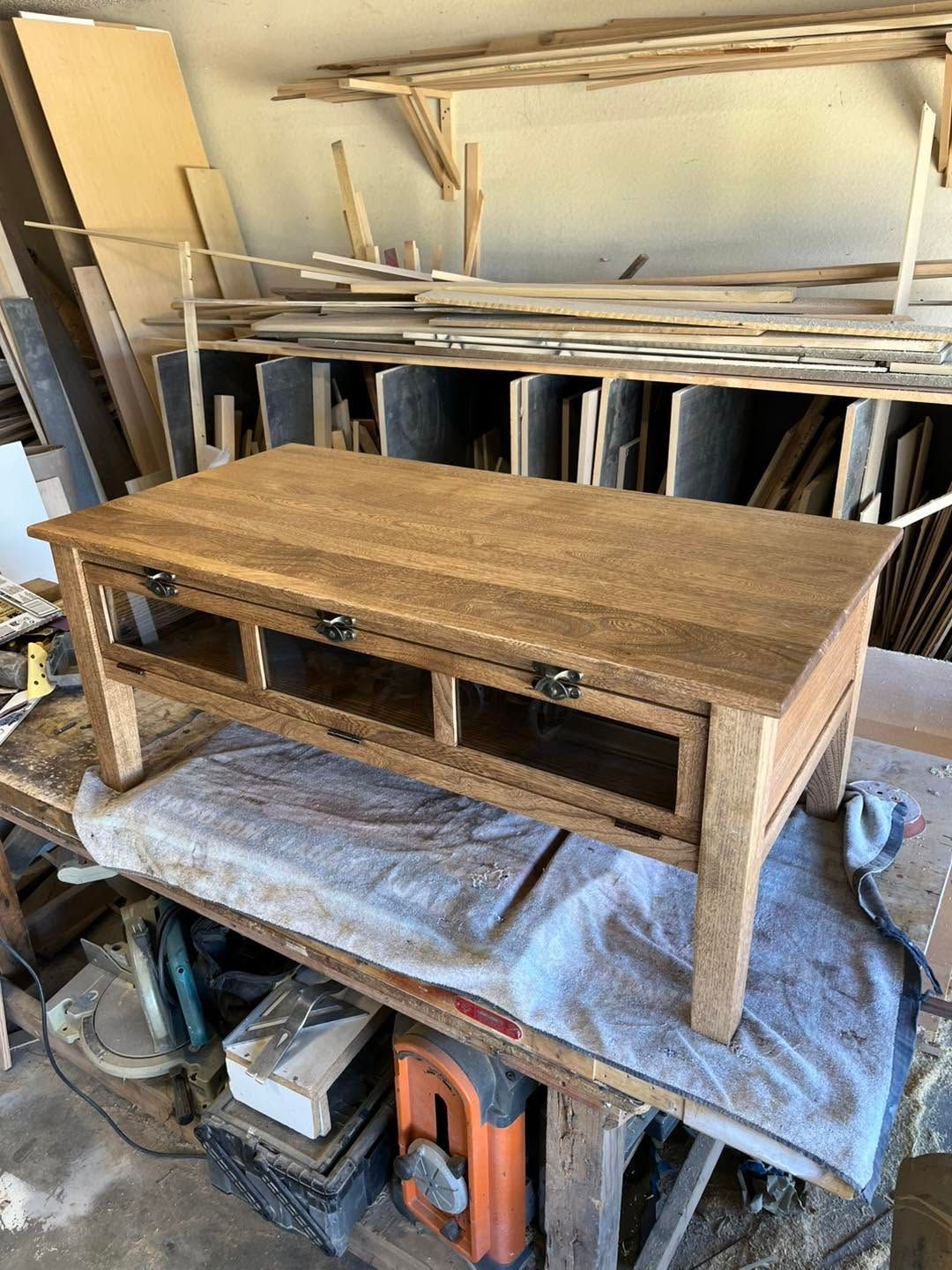 Wooden table on a workbench in a cluttered woodworking shop with stacked boards behind it