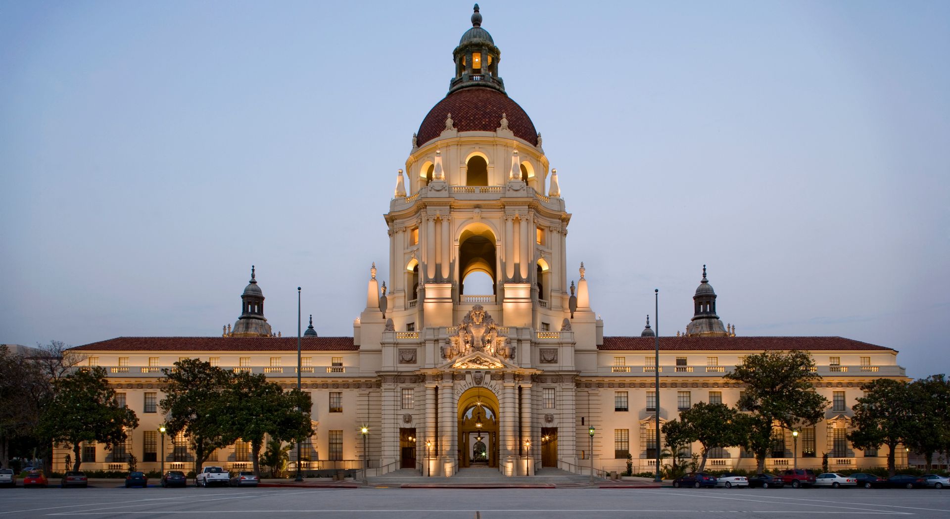 Illuminated historic palace with a central dome at dusk, seen from a wide front view.