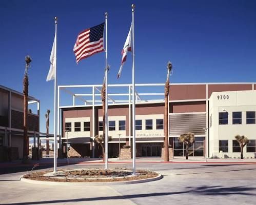 Courtyard of a school building with flagpoles and a U.S. flag in front under a clear blue sky