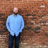 A man with a beard is standing in front of a brick wall.
