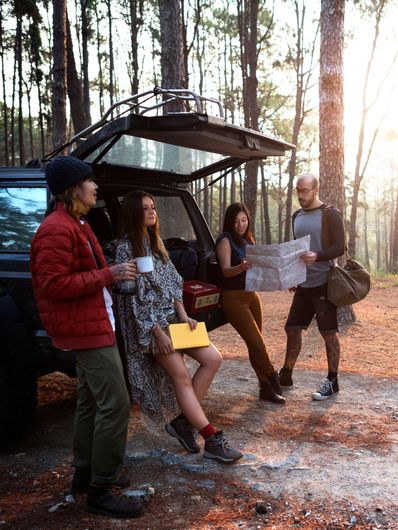 A group of people are standing around a car in the woods.