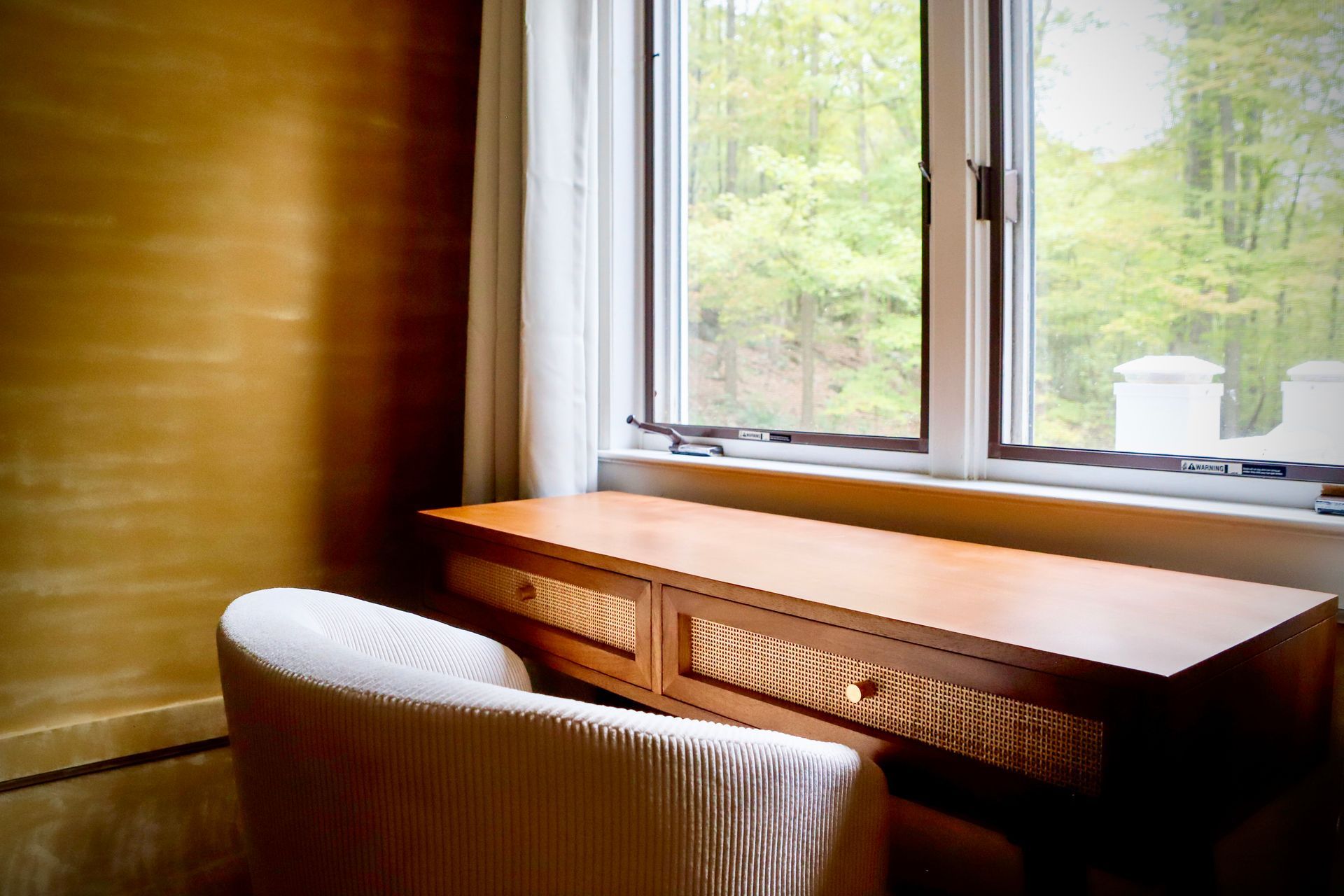 A chair is sitting next to a wooden desk in front of a window.