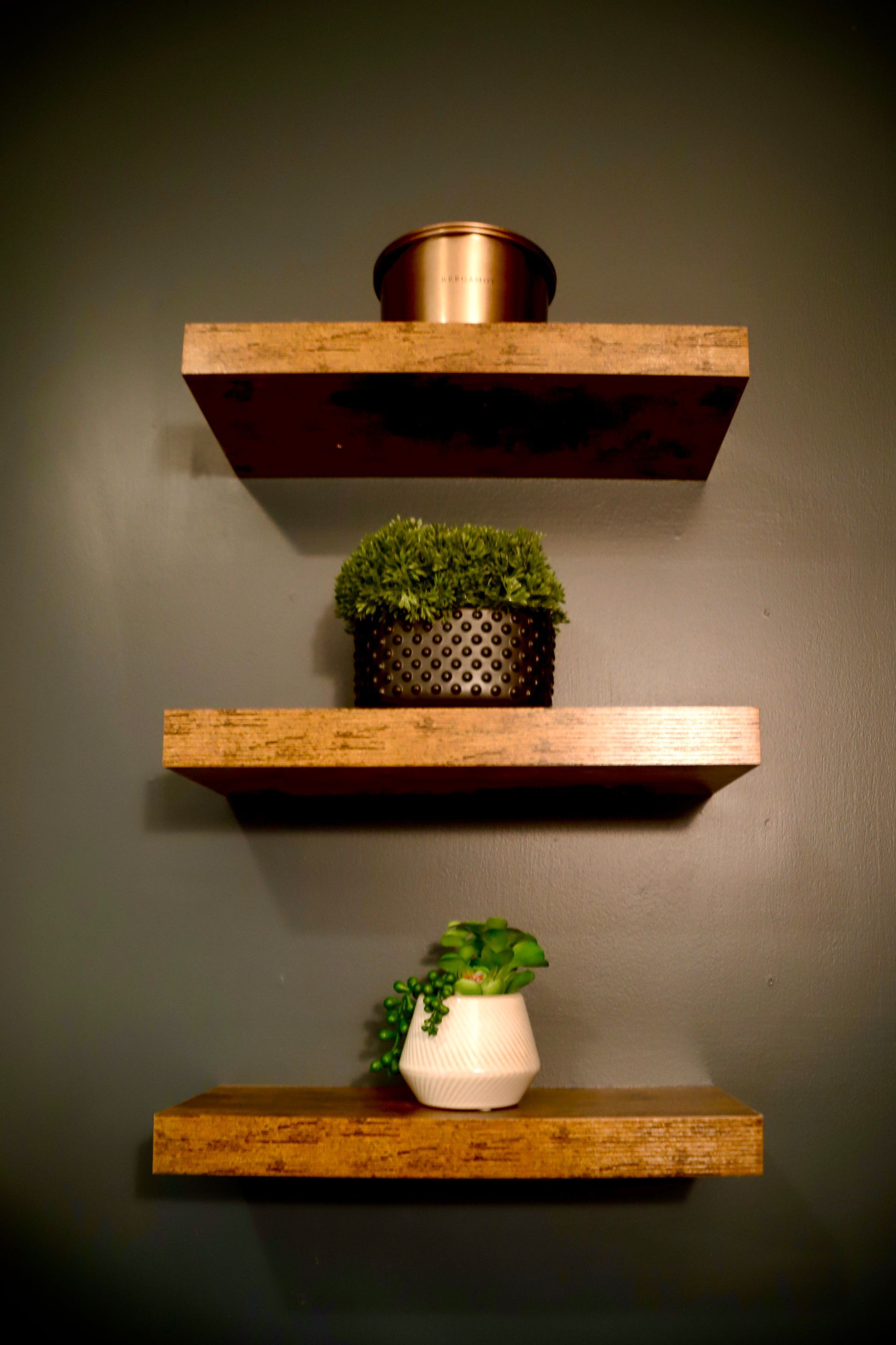 Three wooden shelves hanging on a wall with potted plants on them.