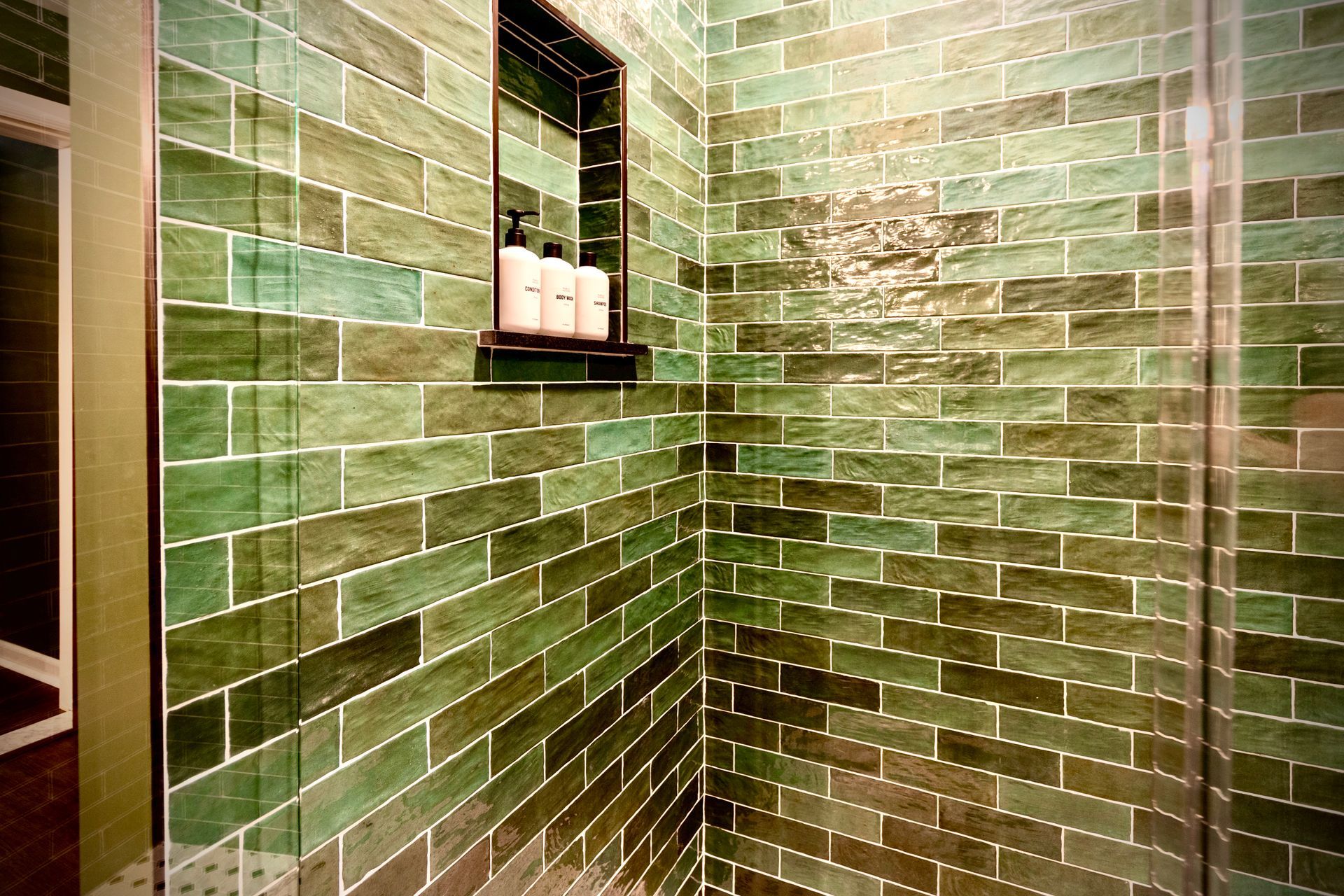 A bathroom with green tiles and a glass shower door.