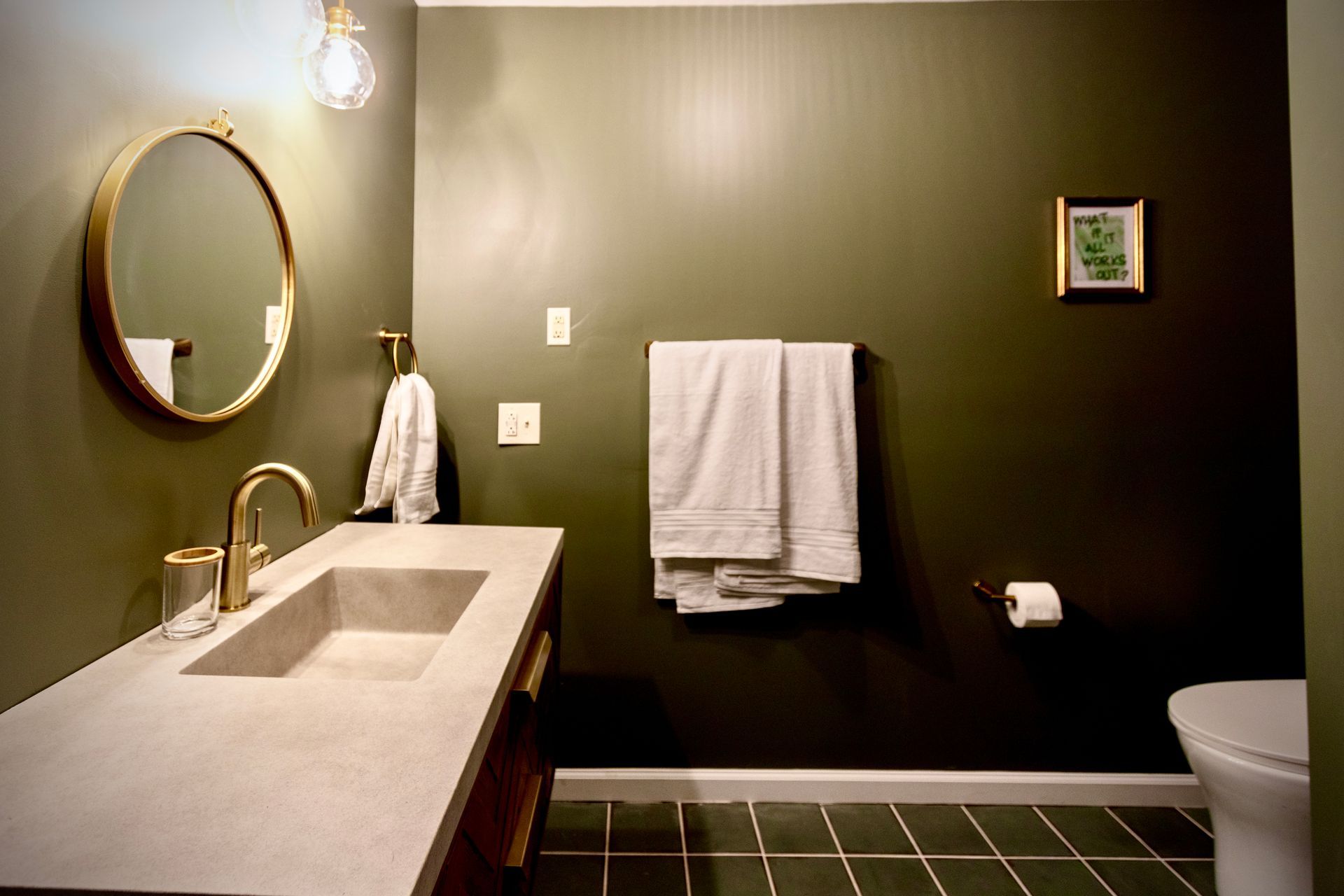 A bathroom with a sink , toilet , mirror and green walls.