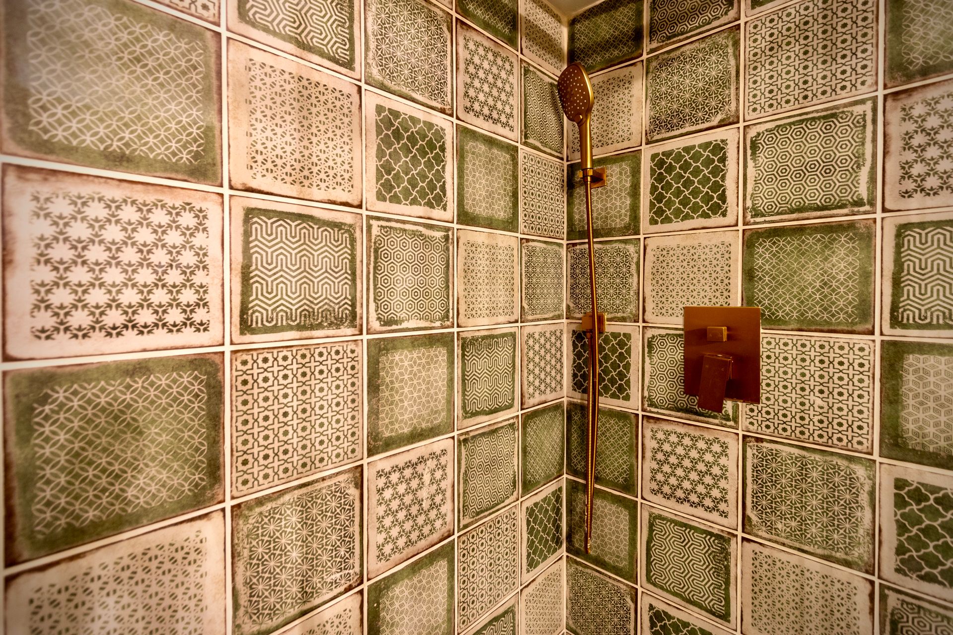 A bathroom with green and white tiles and a shower head.