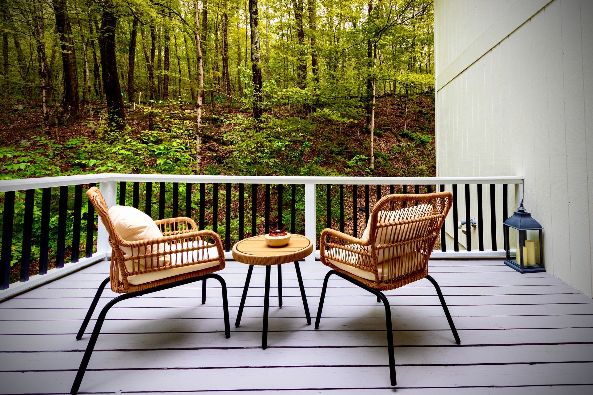 Two chairs and a table on a deck with a forest in the background.