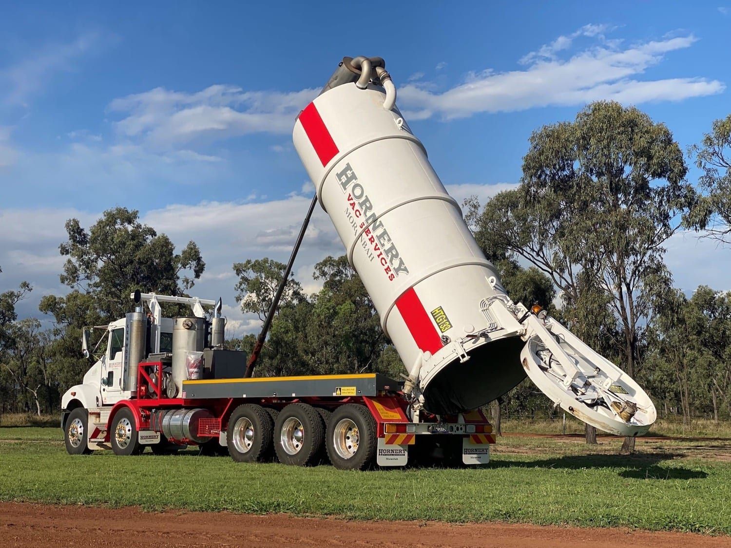 a large white truck with a red stripe on the side is parked in a grassy field .