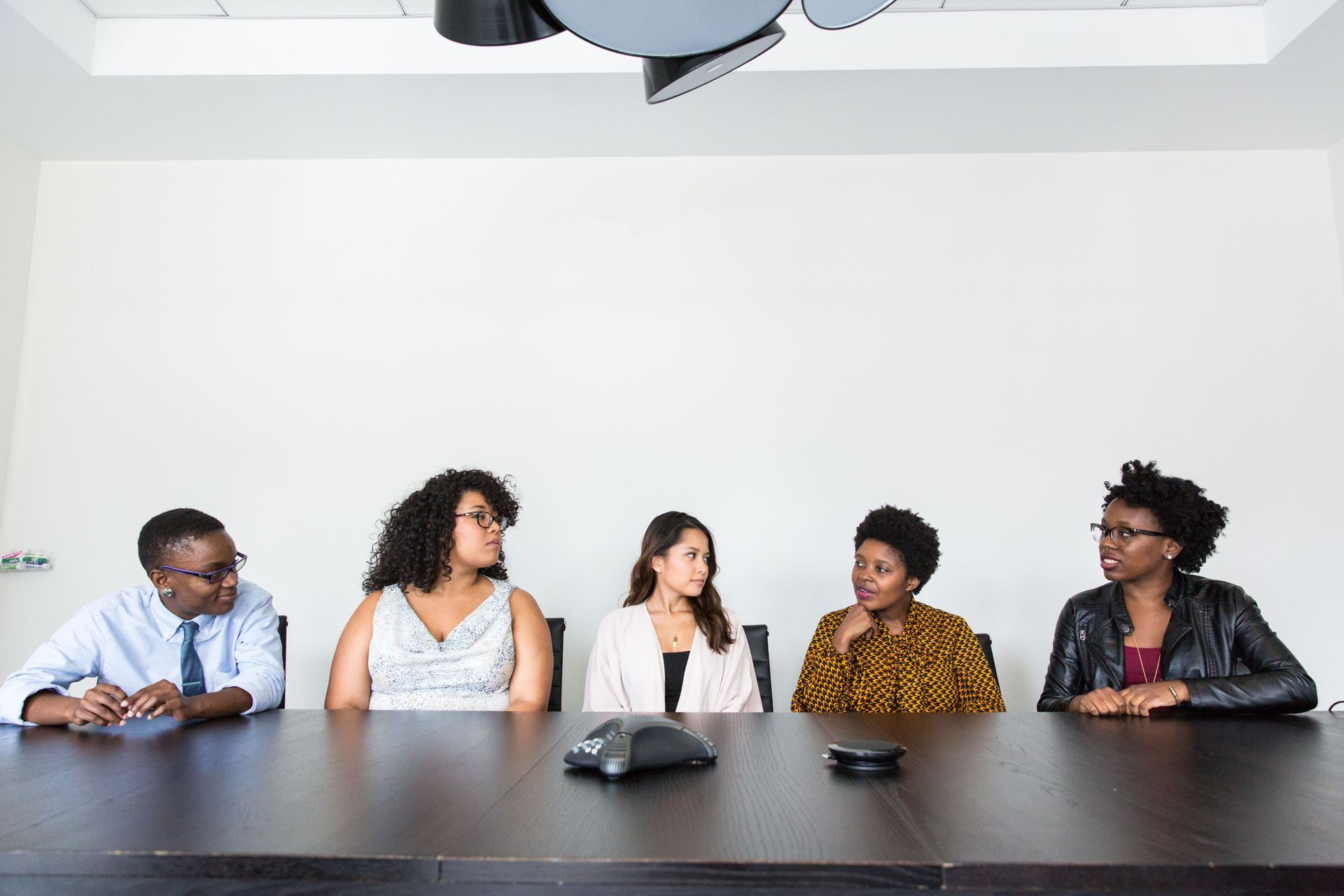 Five people seated at a conference table in a meeting room, looking toward each other.