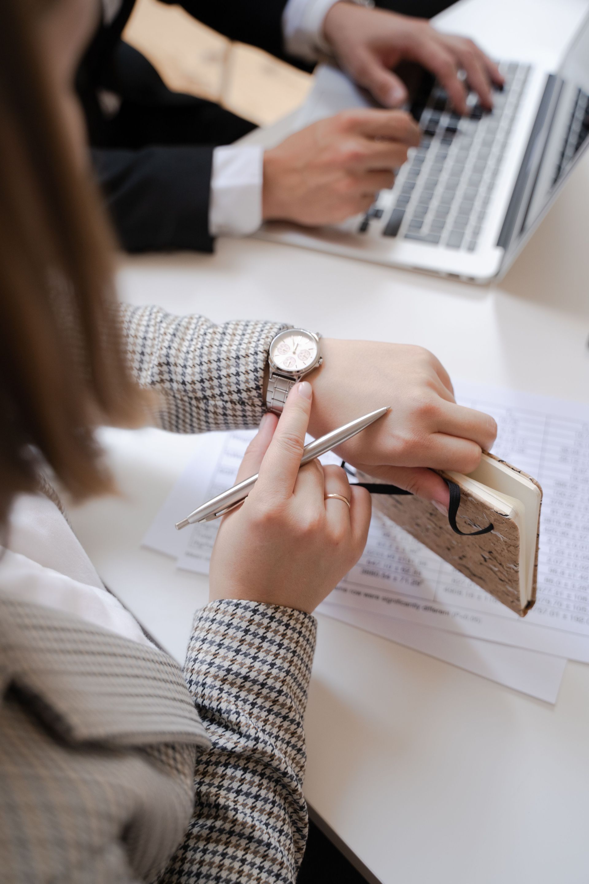 People taking notes at a desk with a laptop and notebook in a meeting setting