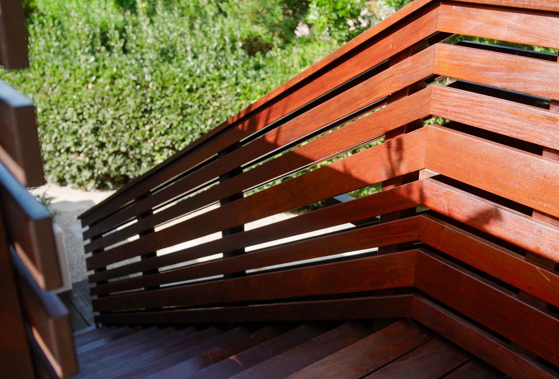 Wooden outdoor staircase with modern railing design, leading to steps, set in a sunny garden.