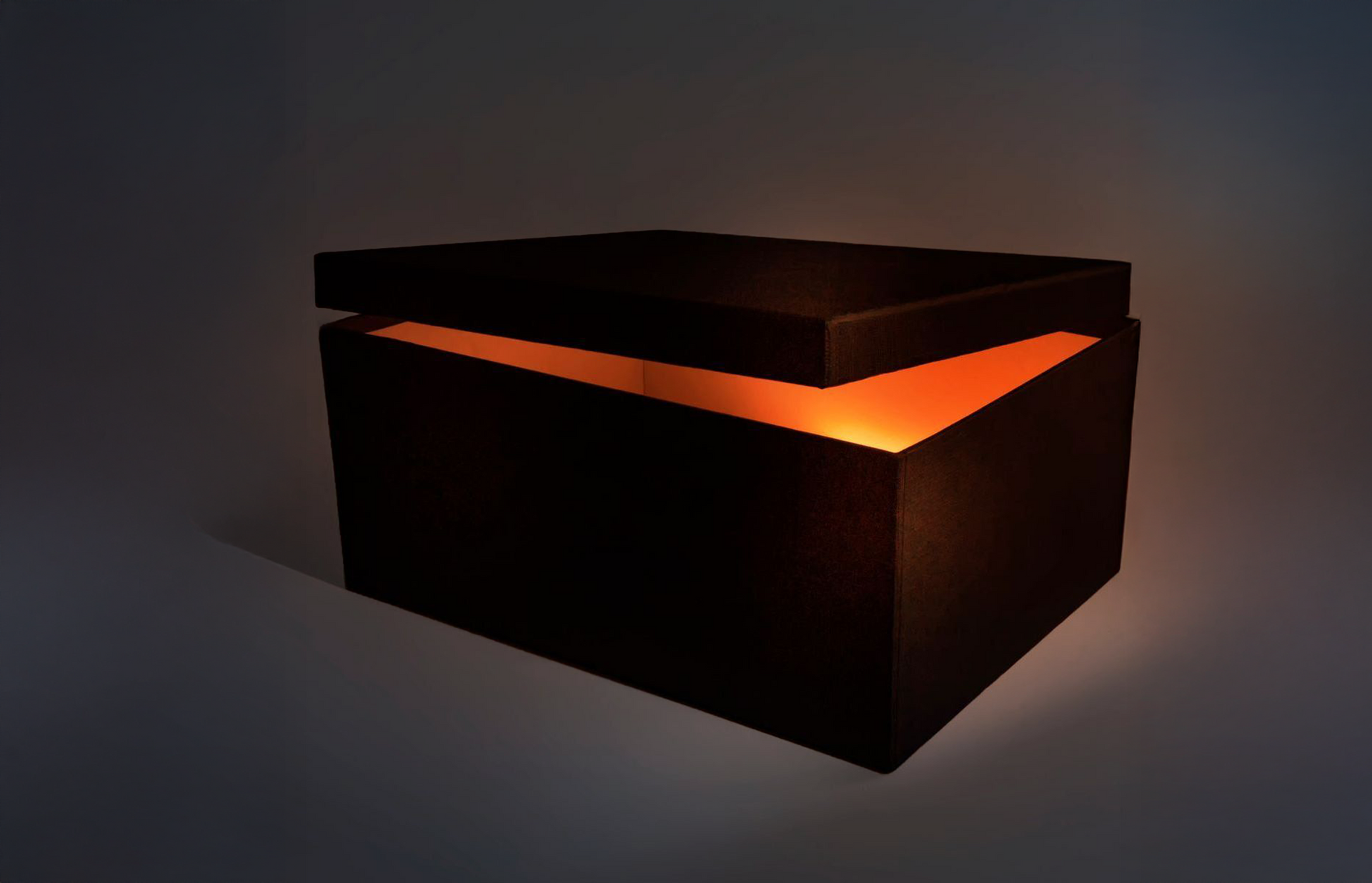 A dark, rectangular box slightly open with a warm, glowing orange light emanating from inside against a gray background.