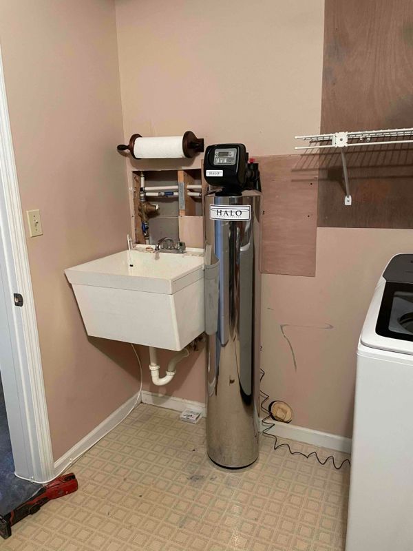 Wall-mounted sink and chrome utility dispenser in a small utility room with beige walls.