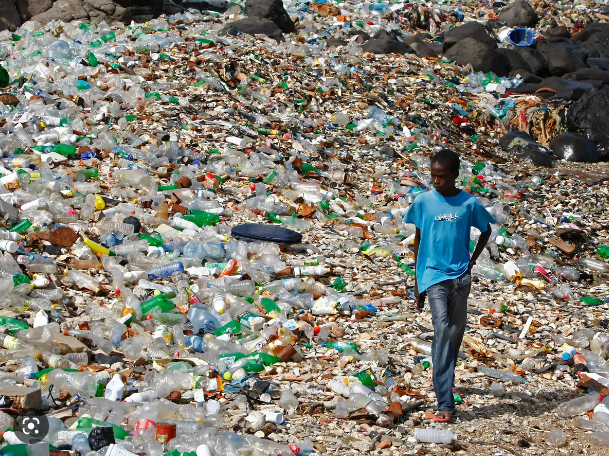 A person in a blue shirt walks through a large trash-strewn landfill.