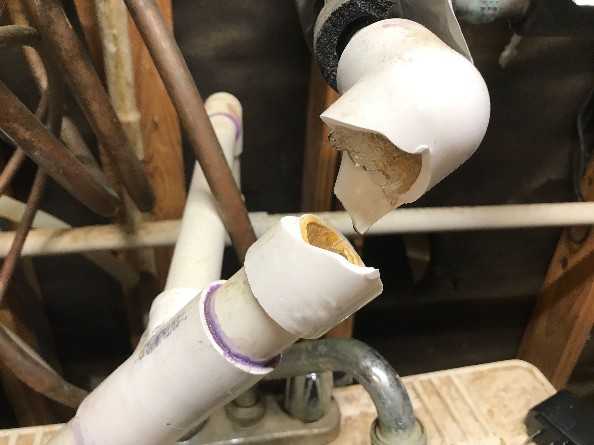 Broken white PVC pipe with exposed interior and loose fittings near metal plumbing