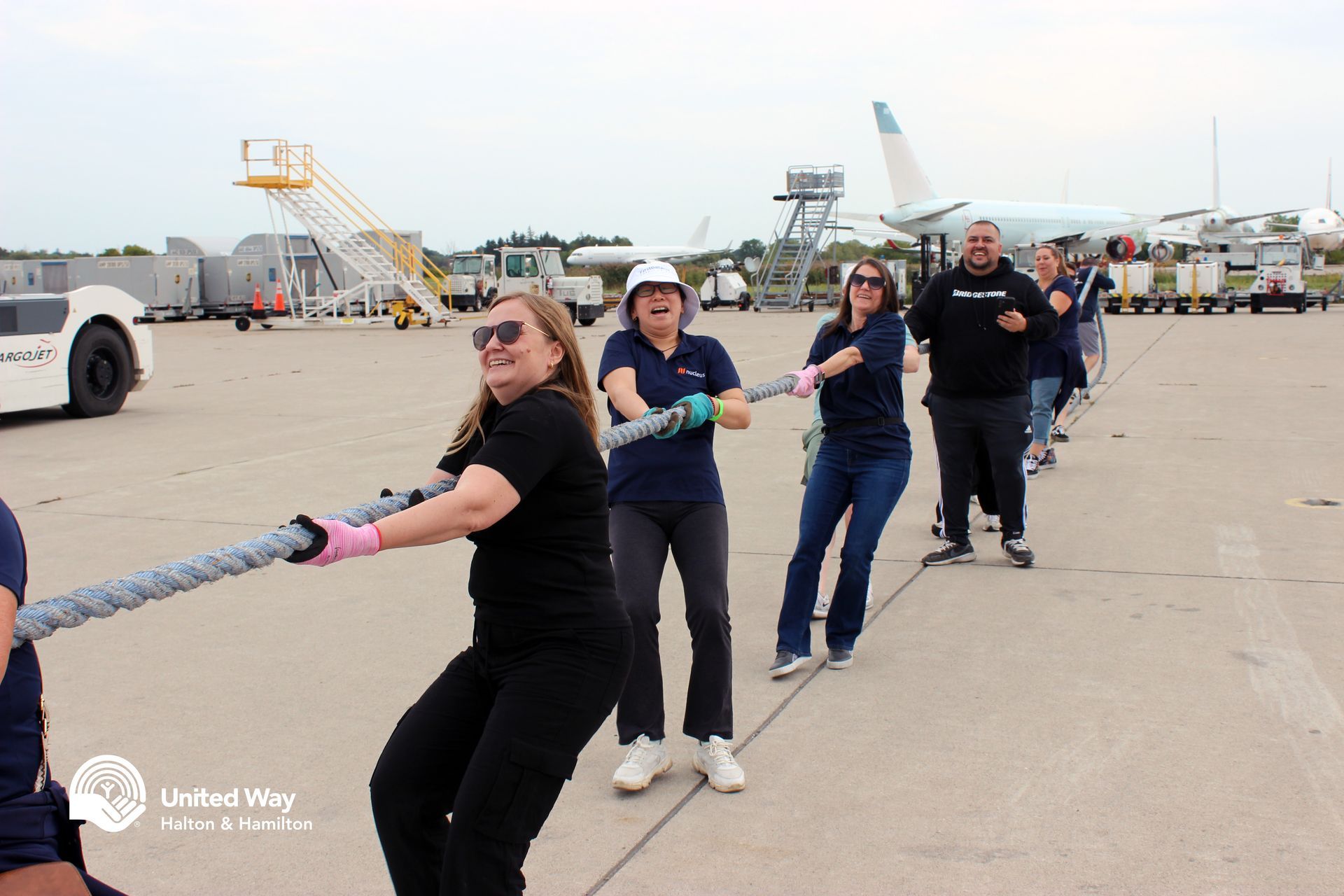 People pulling a large rope in a tug-of-war on an airport tarmac