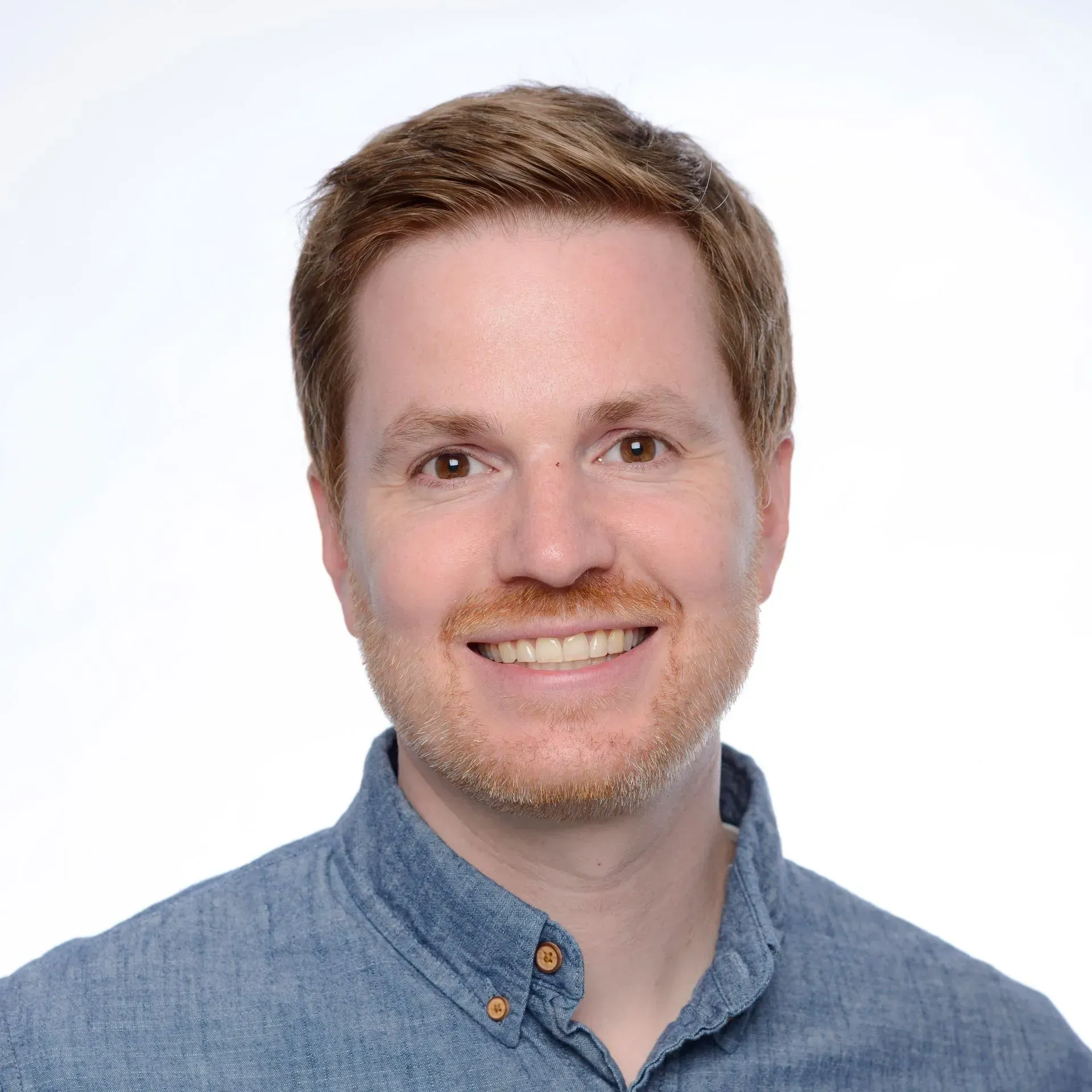 Smiling man in a blue button-up shirt against a white background