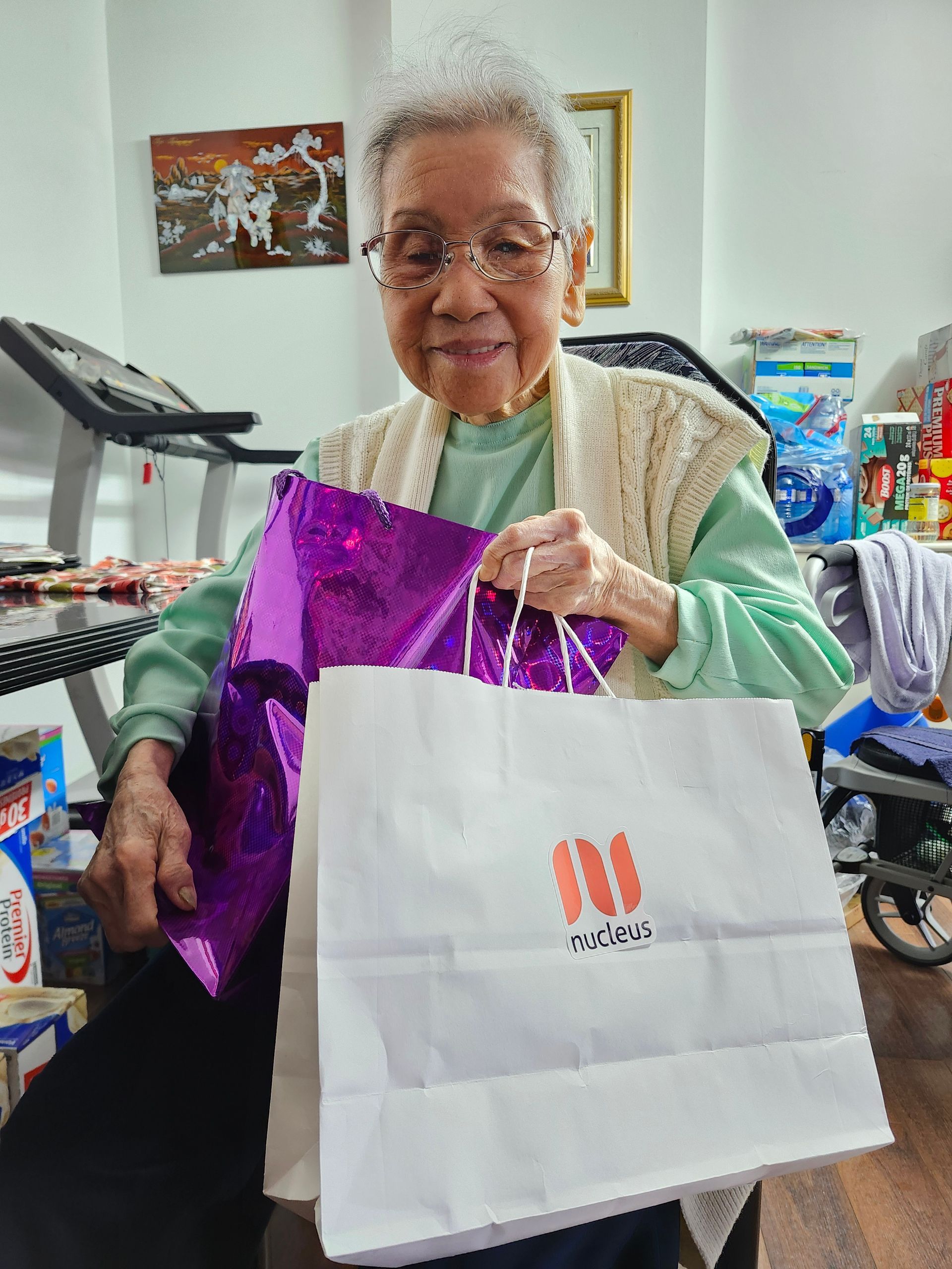 Smiling woman holds a white shopping bag and purple gift bag indoors.