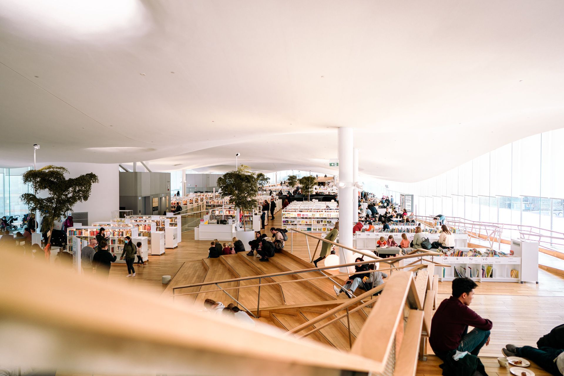 Bright, modern café with tables, plants, and people seated in a spacious indoor lounge