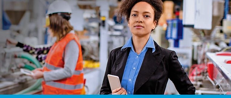 A woman is standing in a factory holding a tablet.