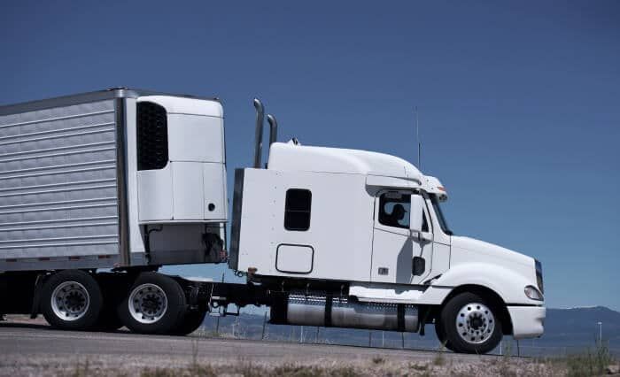 A semi truck is driving down a road with a trailer attached to it.