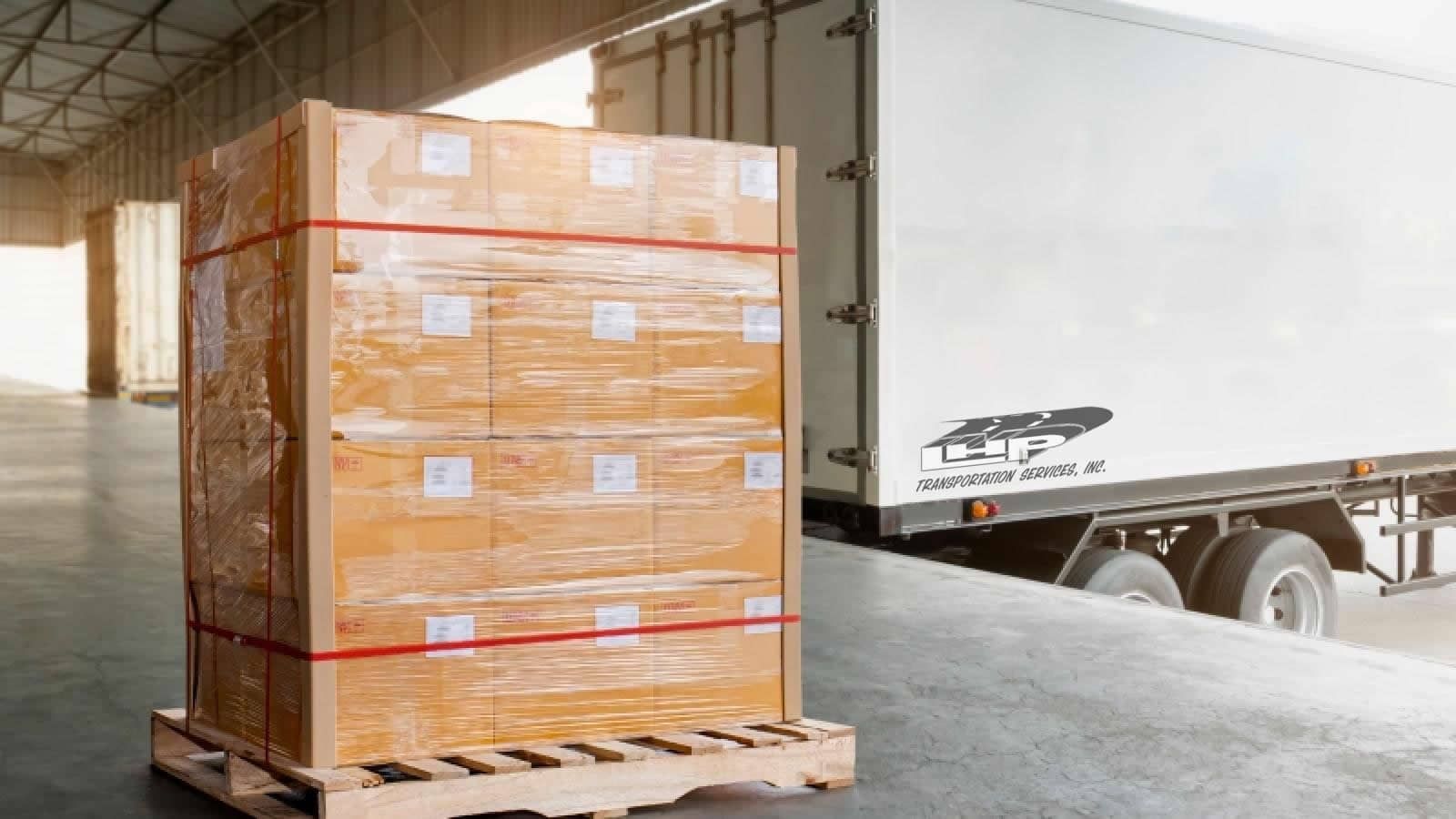 A stack of boxes on a wooden pallet next to a truck in a warehouse.