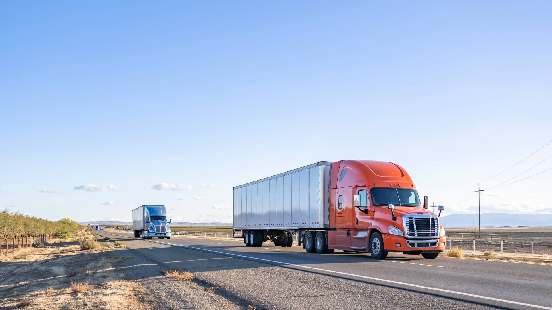 Two semi trucks are driving down a highway in the desert.